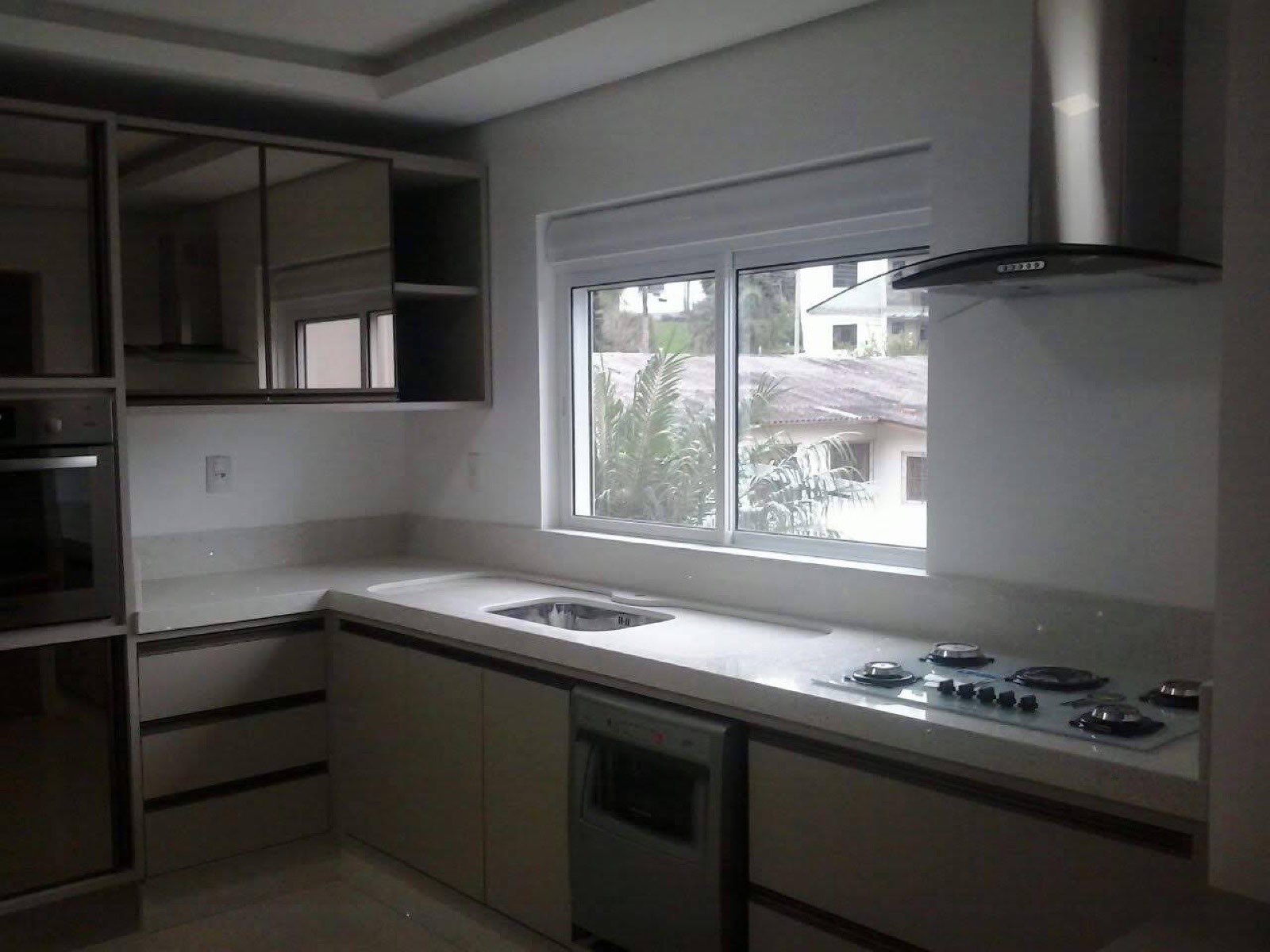 Cozinha em L com bancada em mármore claro, cooktop embutido e cuba, janela ampla